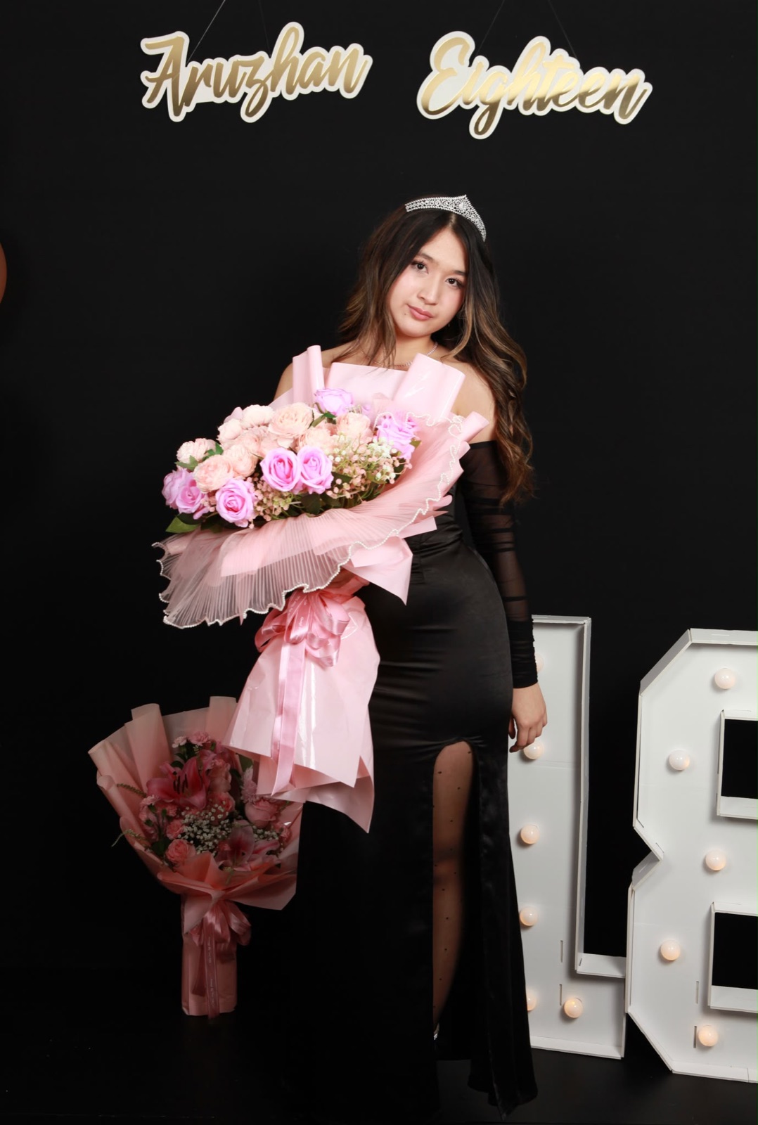 Birthday girl in a black dress with a bouquet at the black Lazuro photo stage